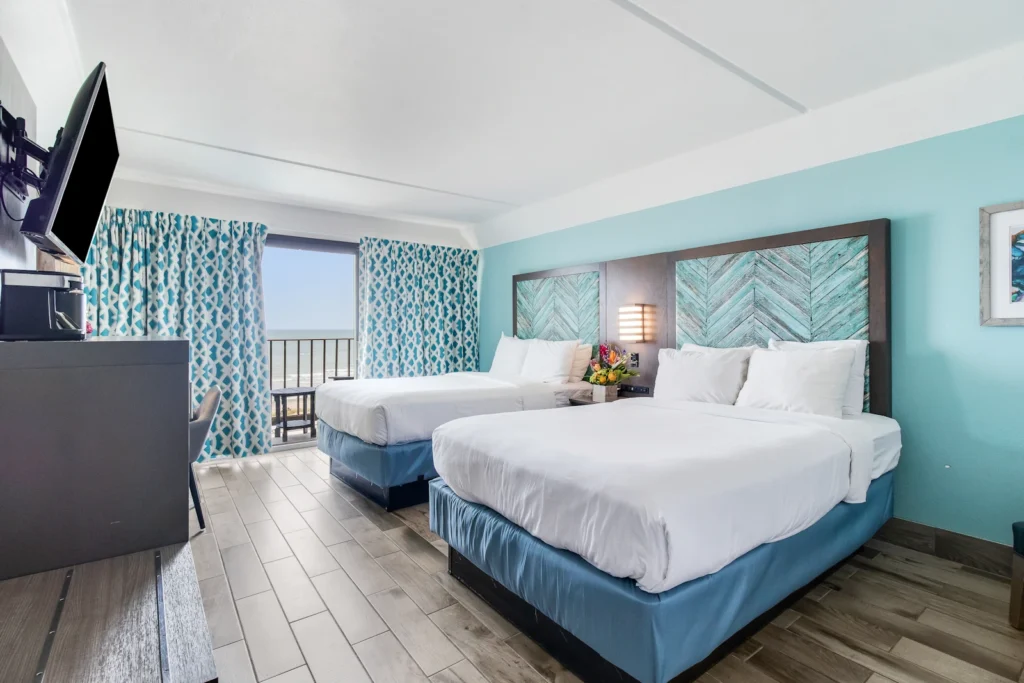 luxurious coastal themed bedroom with a two standard sized bed, washed grey wooden furniture, facing a large sea green accent wall, with patterned curtains in the background shading an oceanfront view