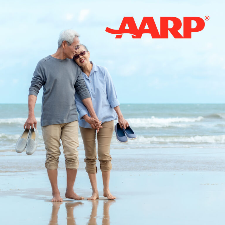 an elderly couple walks through the wet sand of the beach, barefoot and holding each other's hand. in the foreground is red text that reads "AARP"