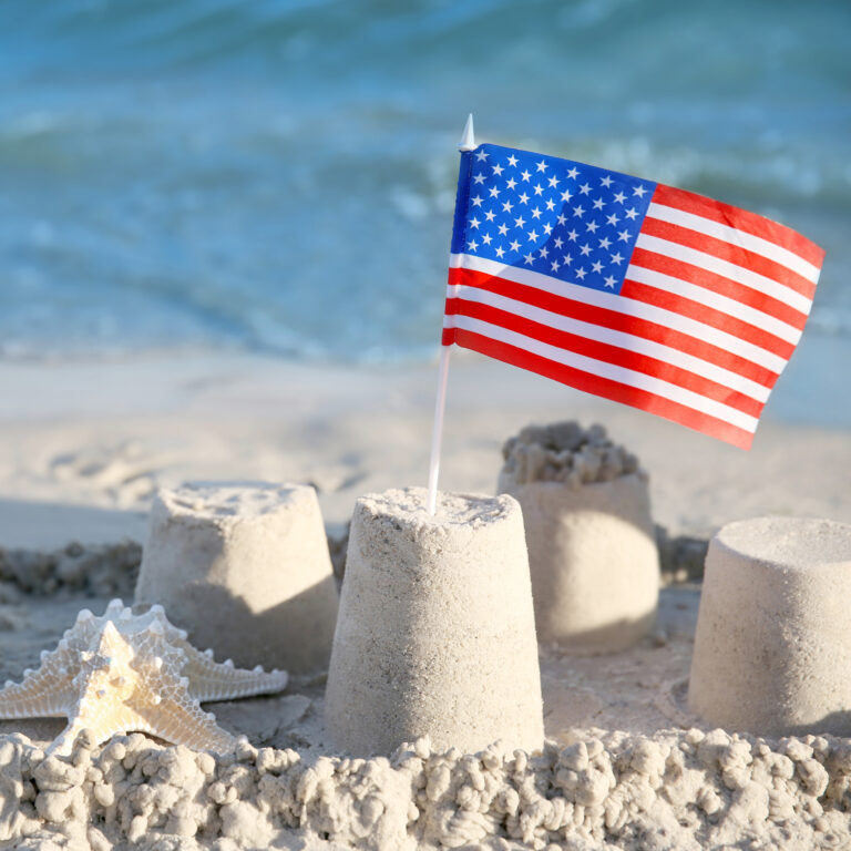 a starfish lays in the sand near a sand castle that is topped with a plastic American flag