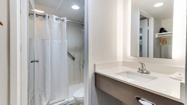 an all-white bathroom with a sink, mirror, toilet, curtained shower, and fluorescent lighting