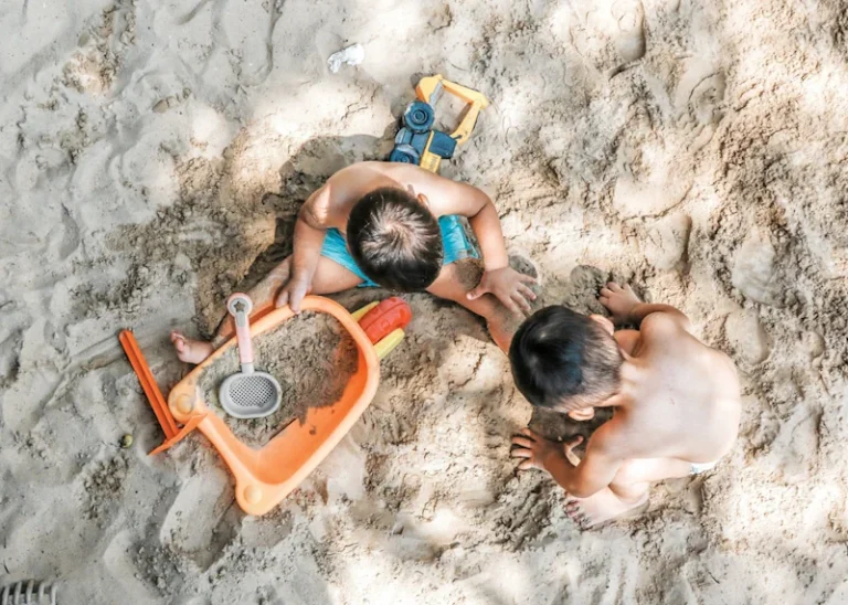 two kids play in the sand with plastic toys