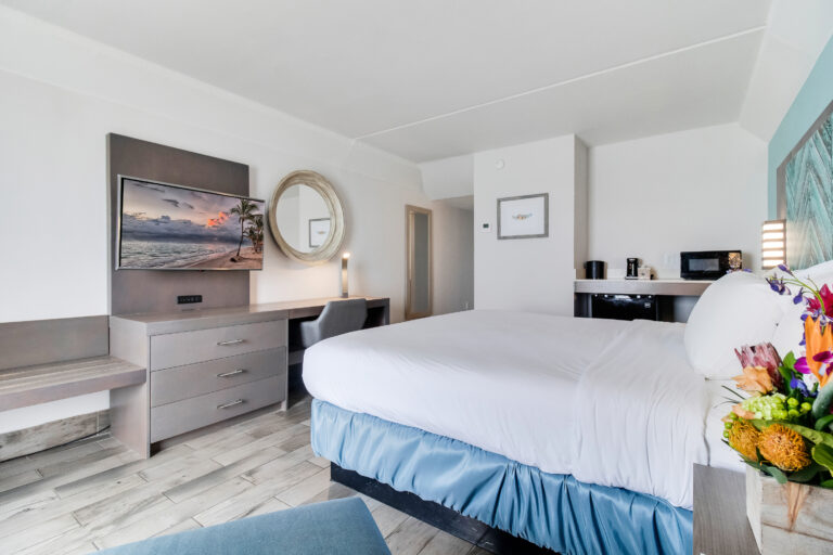 luxurious coastal themed bedroom with a junior king sized bed, washed grey wooden furniture, and sea green accents with a large golden mirror