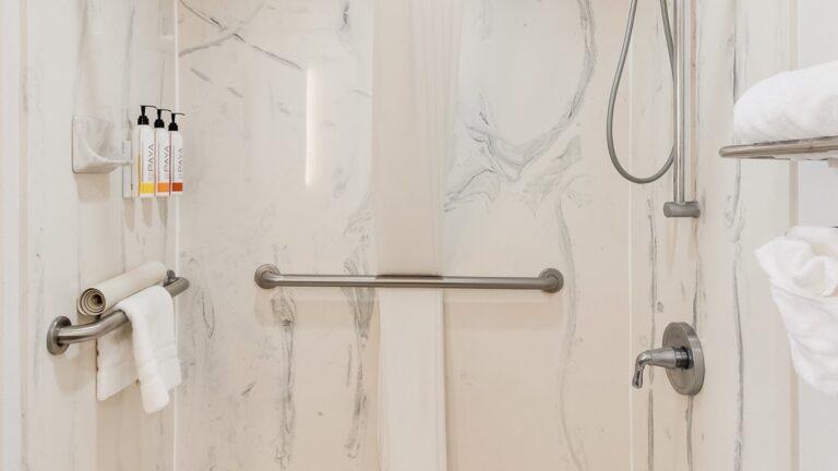 marble lined shower with a silver polished shower, railings, and pipes.
