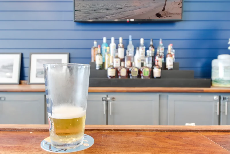 a frosty glass of beer sits on a dark wooden counter facing polished metal taps and alcohol bottles.