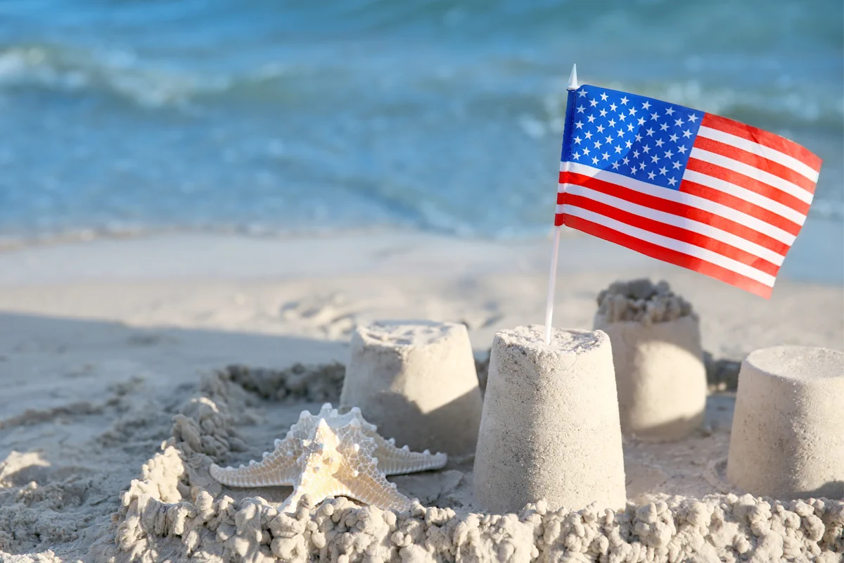 a starfish lays in the sand near a sand castle that is topped with a plastic American flag