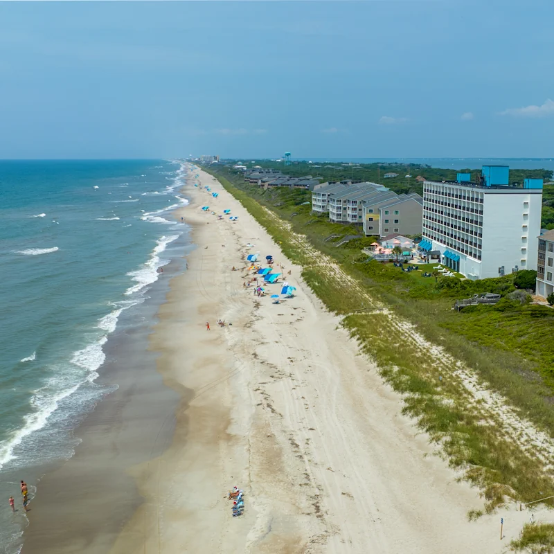 a high altitude drone shot of the crystal coast oceanfront shoreline beach, stretching for miles with the crystal coast oceanfront hotel in the foreground