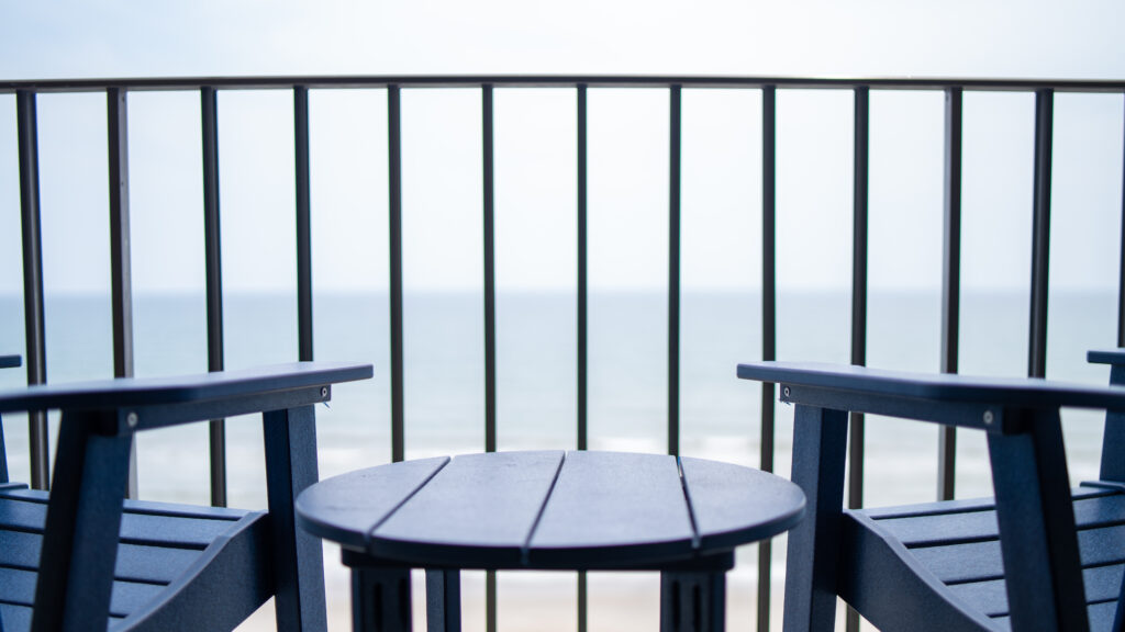 a close-up shot of two wooden blue chairs sitting on a hotel room balcony facing the ocean waters